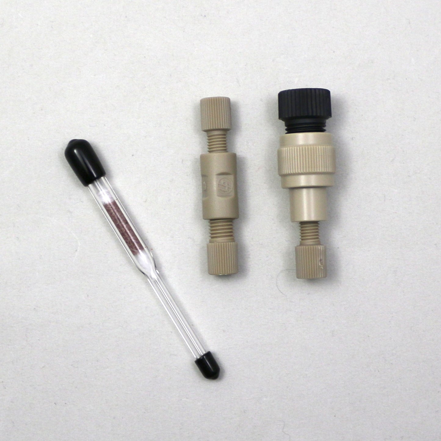 Two mechanical components and a clear tube with black caps on a light gray background