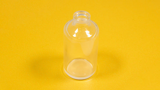 A clear glass bottle resting on a bright yellow surface, showcasing its transparency and shape.