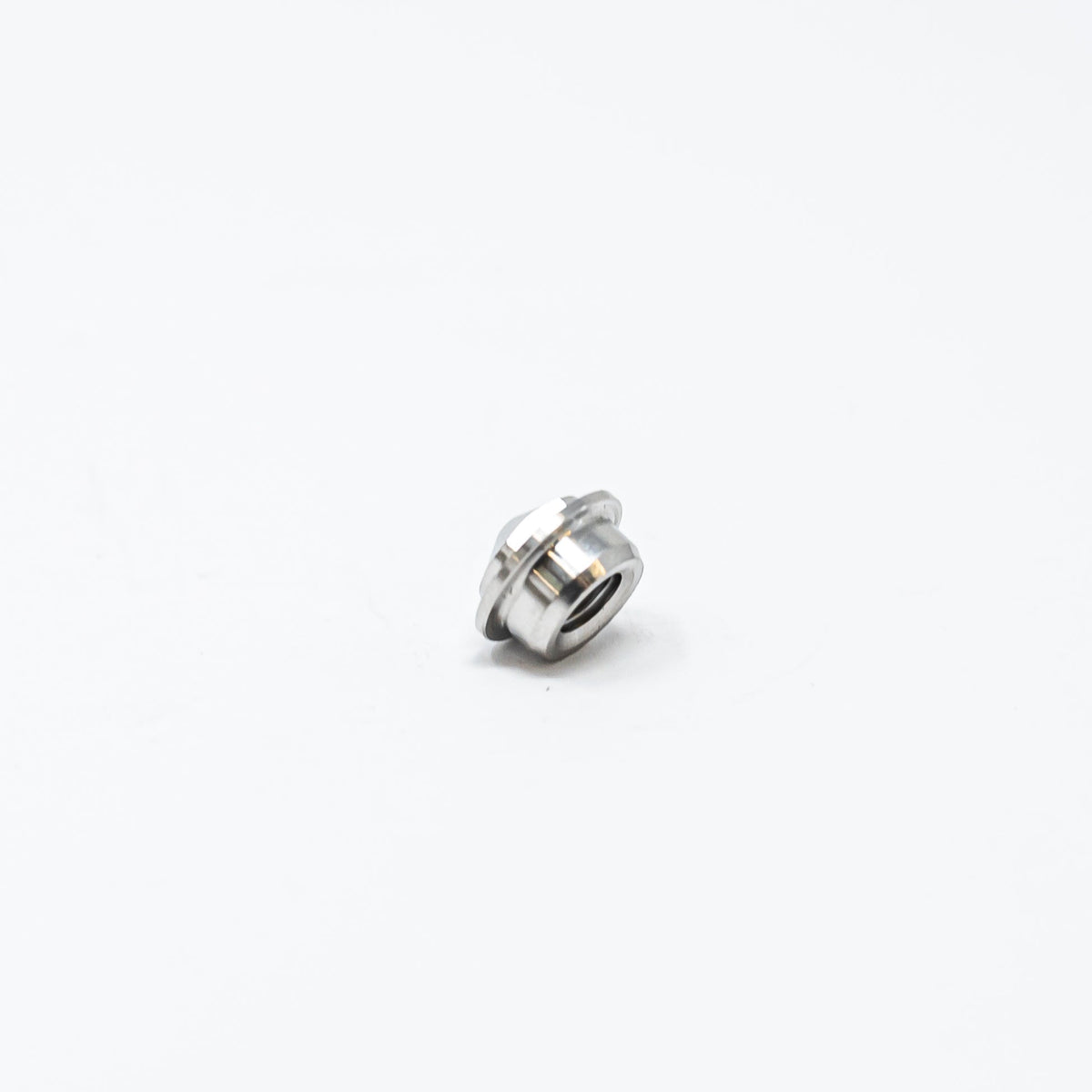 A small metal nut resting on a clean white surface, showcasing its shiny texture and circular shape.