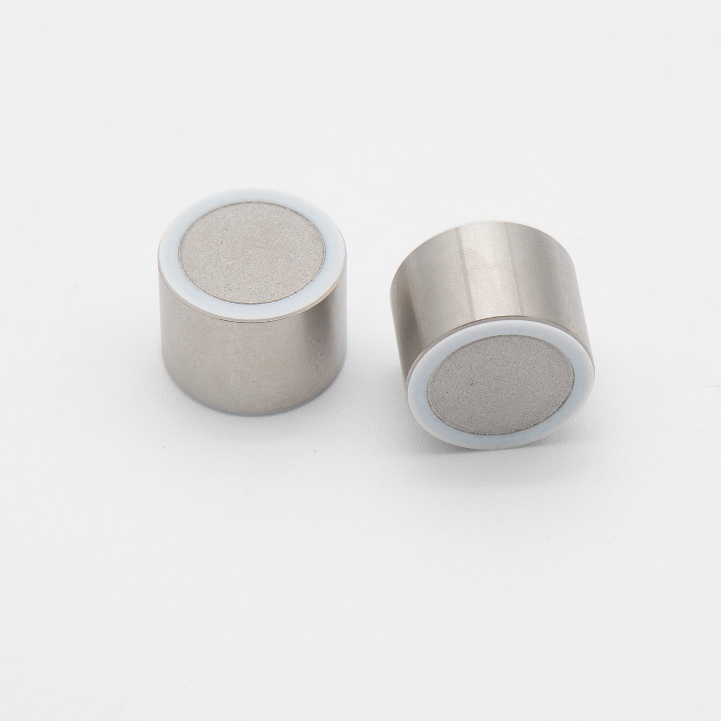 A pair of small metal cylinders adorned with white circles, displayed together, highlighting their simple yet distinct design.